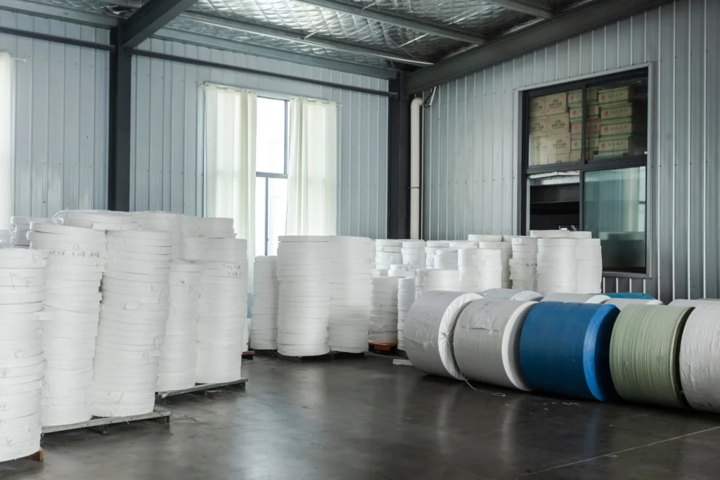 Stacked woven fabric rolls stored in an FIBC bulk bag manufacturing facility, ready for production.