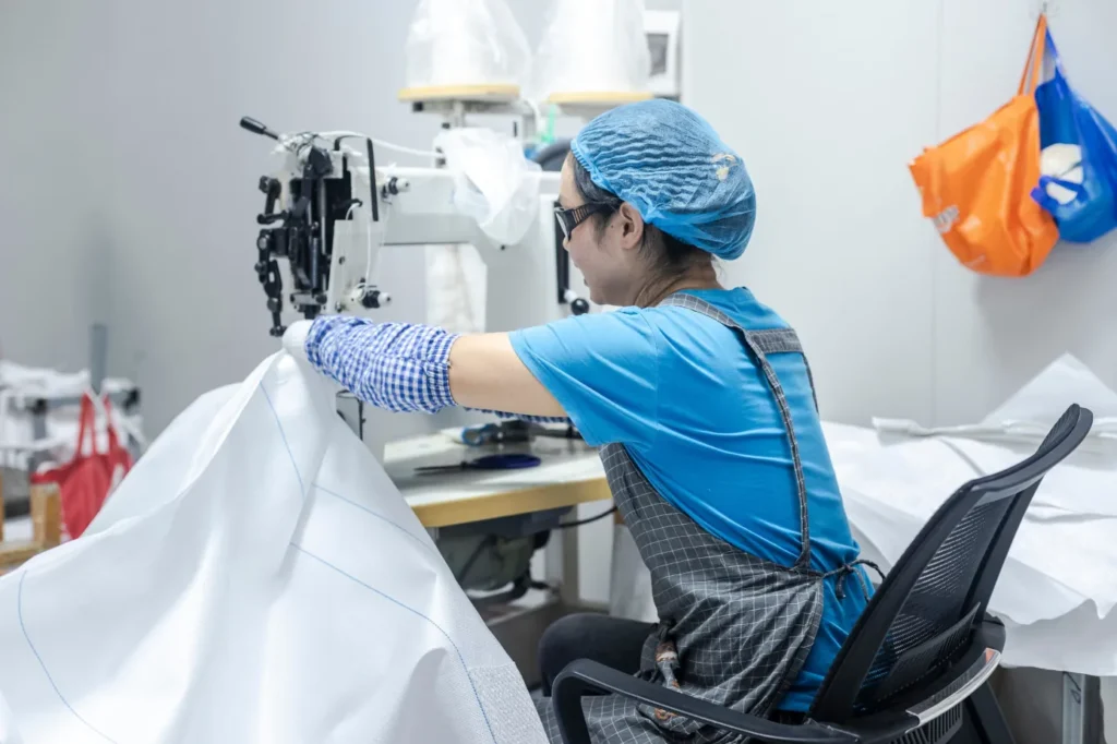 A female worker in protective gear sewing FIBC bulk bag in a factory setting
