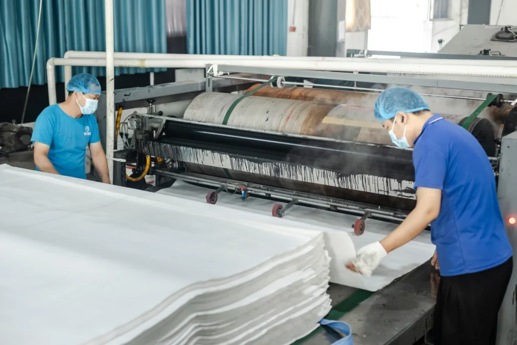 Workers processing woven fabric for FIBC bulk bags using an industrial printing machine.